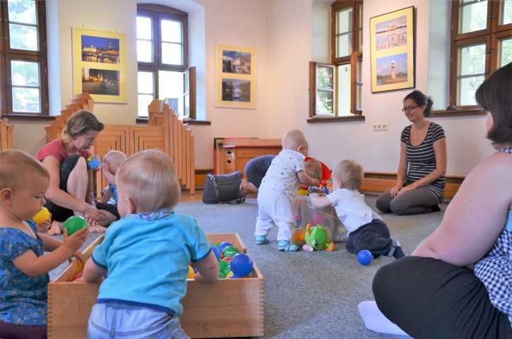 Kursbild Eltern-Kind-Gruppe - Kinder spielen in einem Raum, Eltern sitzen am Rand