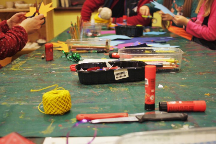 Kursbild Kreativwerkstatt - Leim, Messer, Strick, Boxen mit Stiften und Bastelmaterial sind zu sehen. Im Hintergrund sind Kinderhände die Objekte halten.