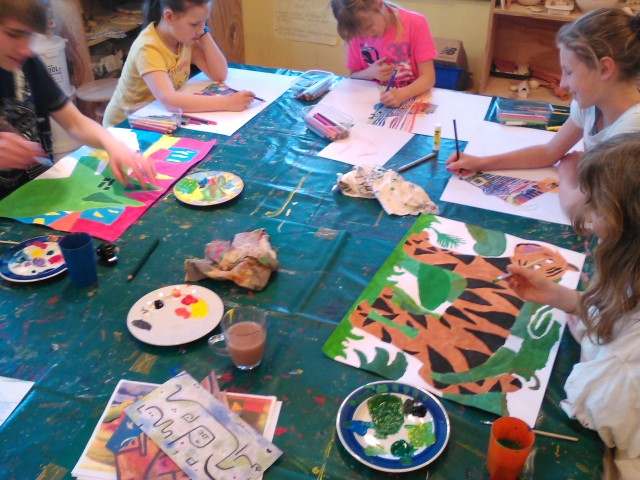 Kursbild Malen und Zeichnen - Kinder sitzen um einen Tisch. Vor ihnen liegen bunte Bilder. Sie halten Stifte oder Pinsel in der Hand.